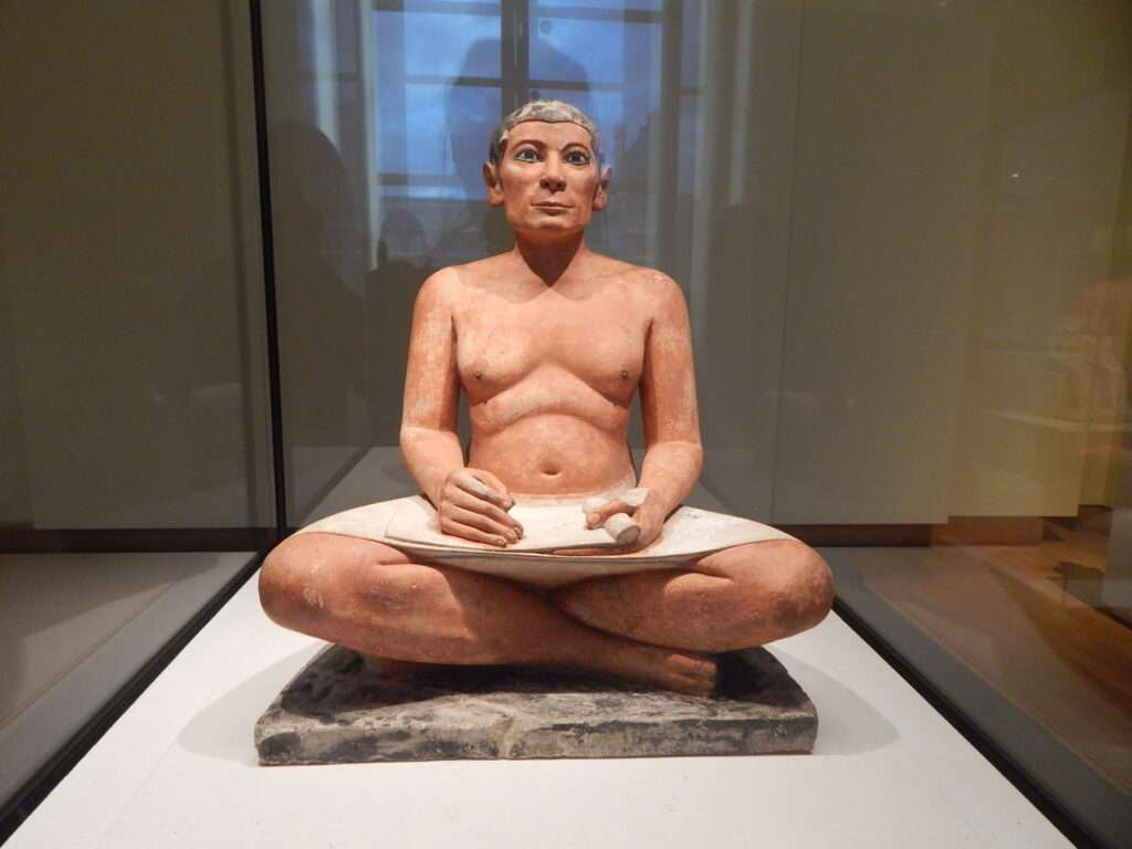 The seated scribe depicts a man sitting with a paper on his lap.